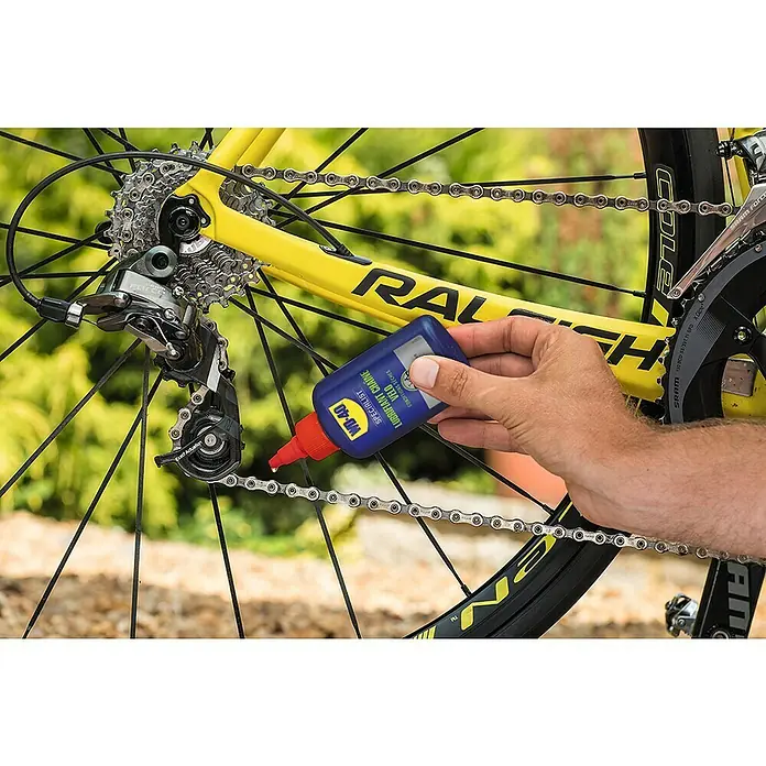 WD-40 Bike Aceite para cadenas Ambiente Seco - 100 ml - Se está aplicando un lubricador de cadena Velo Specialist WD-40 azul a una cadena de bicicleta para mejorar el rendimiento.
