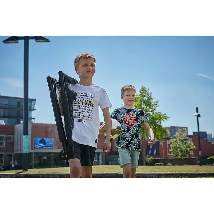 Salta Fußballtor - 100 x 60 x 60 cm, Schwarz, 2 Stk. - Ein Junge trägt ein zusammengeklapptes schwarzes tragbares Sporttor im Freien, bereit zum Spielen mit einem Fußball.