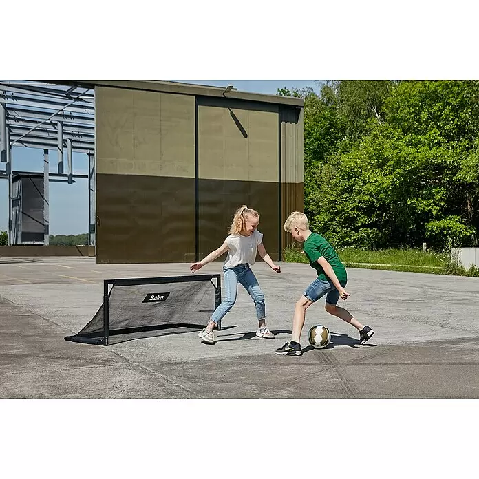 Salta Fußballtor Techniq - 150 x 60 x 60 cm, Schwarz - Schwarzes Salta Minitor, das von zwei Kindern zum Fußballspielen auf gepflastertem Untergrund genutzt wird.