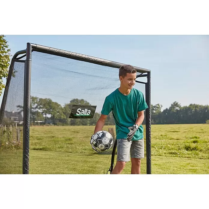 Salta Fußballtor - 220 x 80 x 170 cm, Schwarz - Junge hält Fußball und trägt Handschuhe vor einem schwarzen Salta Fußball-Rebounder mit Netz.