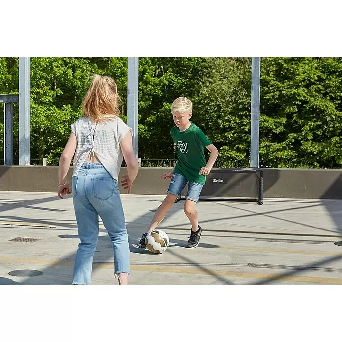 Salta Fußballtor Techniq - 150 x 60 x 60 cm, Schwarz - Ein Junge dribbelt einen weiß-gold-schwarzen Fußball beim Spiel mit einem Mädchen.