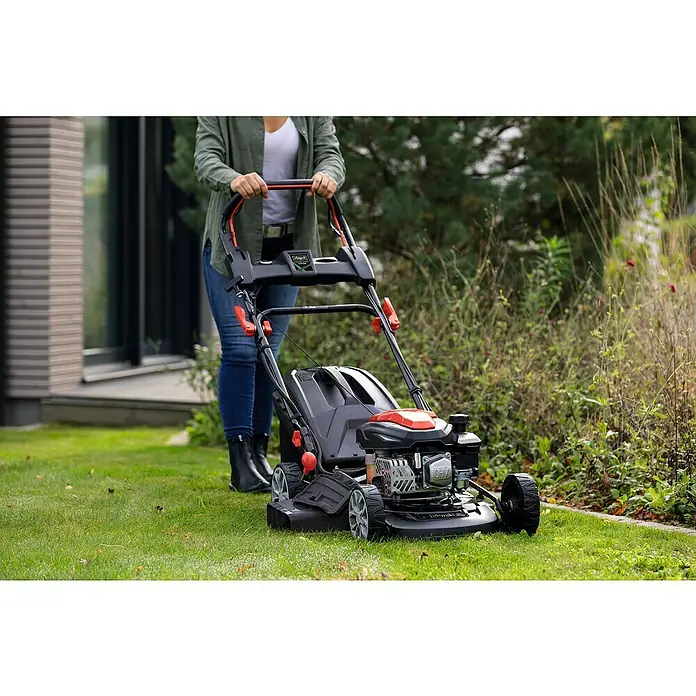 Scheppach Benzin-Rasenmäher PML46-150ES - 150 cm³, Schnittbreite: 46 cm, Hybrid-Start: Elektrostart & Seilzugstarter - Eine Person benutzt einen Scheppach Benzin-Rasenmäher auf einem Rasen. Der Rasenmäher ist schwarz und rot.