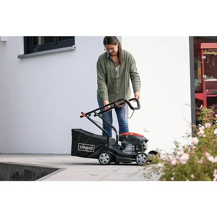 Scheppach Benzin-Rasenmäher PML40-132P - 2,4 kW, 131 cm³, Schnittbreite: 40 cm - Eine Frau bedient einen Scheppach Rasenmäher mit Grasfangkorb vor einem weißen Gebäude.