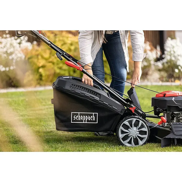 Scheppach Benzin-Rasenmäher PML53-225S - 224 cm³, Schnittbreite: 53 cm, Seilzugstarter - Nahaufnahme eines Scheppach-Rasenmähers mit Fangkorb, der von einer Person bedient wird, auf einer Rasenfläche.