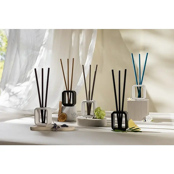 Ipuro Essentials Raumduft Scented SticksWhite Lily, 6 Stk. - Eine Sammlung von quadratischen Raumduftspendern in verschiedenen Farben, die auf einer hellen Oberfläche mit floralen Akzenten präsentiert werden.