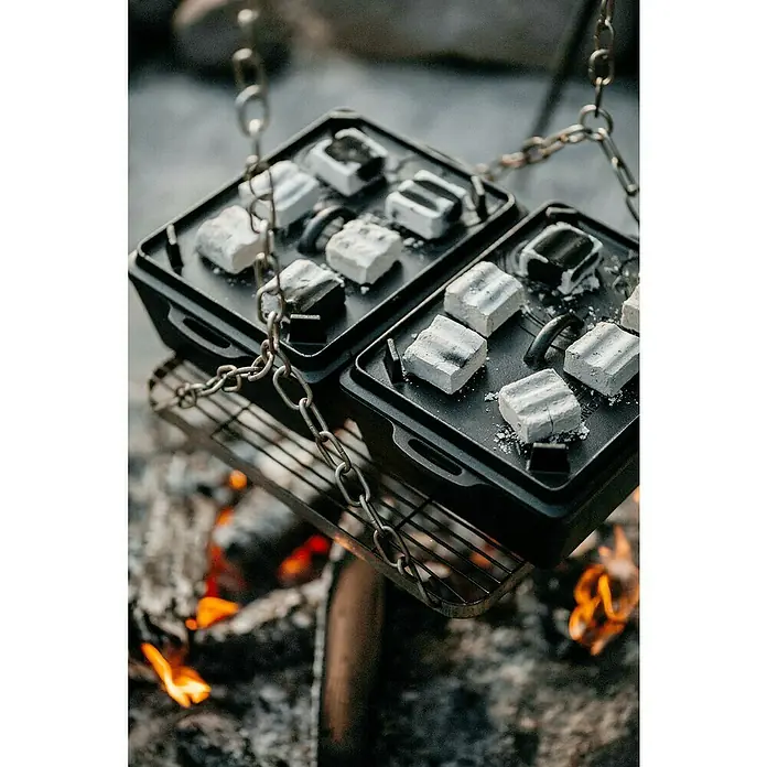 Petromax Auflaufform - L x B x H: 34 x 24 x 14,5 cm, Gusseisen, 4,5 l - Zwei schwarze gusseiserne Kochplatten hängen über einem Lagerfeuer an einer Kette. Auf den Platten liegen Würfel aus Grillkohle.