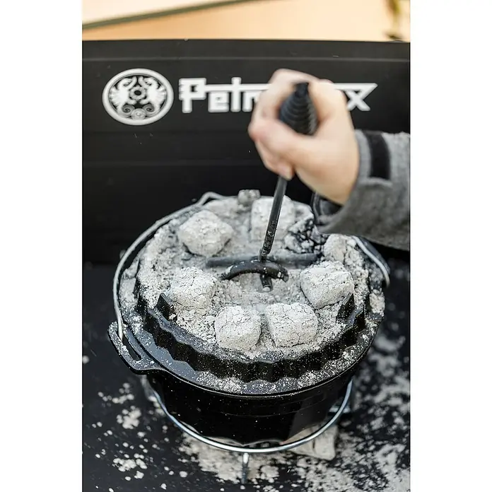 Petromax Deckelheber - Passend für: Dutch Oven Deckel, Länge: 34 cm - Ein Petromax Dutch Oven mit Briketts und Deckelheber, bereit zum Kochen im Freien. Ideal für Camping und Outdoor-Abenteuer.