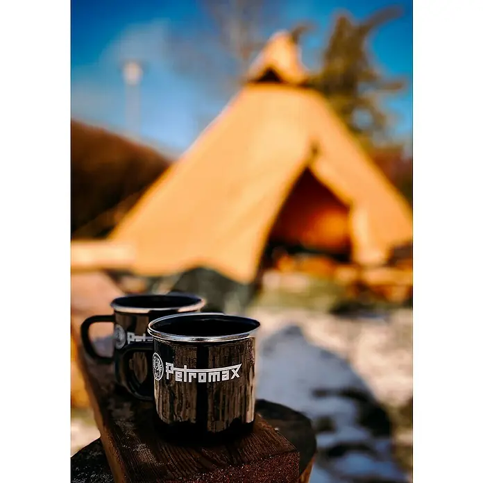 Petromax Tasse - 370 ml, Schwarz - Zwei schwarze Petromax-Emaillebecher auf Holz vor einem Zelt. Perfekt für Outdoor-Abenteuer und Campingausflüge.