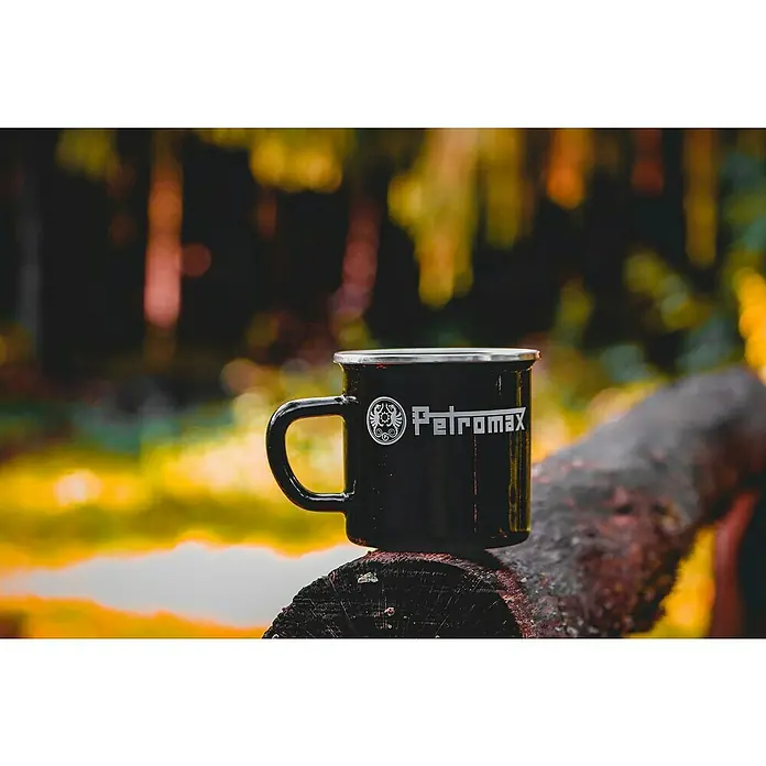 Petromax Tasse - 370 ml, Schwarz - Nahaufnahme einer schwarzen Petromax Emailletasse auf einem Baumstamm. Perfekt für Outdoor-Abenteuer und zum Genießen heißer Getränke in der Natur.