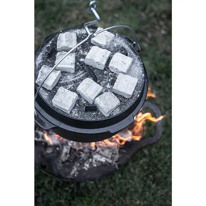 Petromax Dutch Oven - Ø x H: 36,4 x 20 cm, Gusseisen, 5,5 l, Mit Füßen - Ein Dutch Oven hängt über einem Lagerfeuer, der Deckel ist mit Grillkohle bedeckt. Der Dutch Oven eignet sich perfekt zum Kochen im Freien.