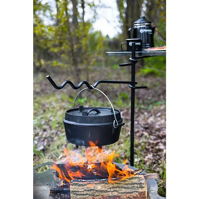 Petromax Dutch Oven - Ø x H: 31 x 18,6 cm, Gusseisen, 3,5 l, Mit Füßen - Ein Dutch Oven hängt über einem Lagerfeuer. Im Hintergrund steht ein Campingtisch mit Kaffeekanne und Tasse.