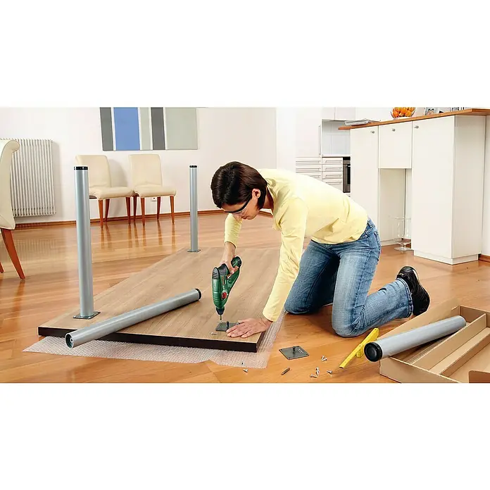 Bosch Power for All 12V Akku-Bohrhammer Uneo - 12 V, 1 Akku, 2 Ah, 0,5 J - Frau montiert einen Tisch mit einer Bohrmaschine. Die silbernen Tischbeine liegen bereit zur Montage auf der Holzplatte.