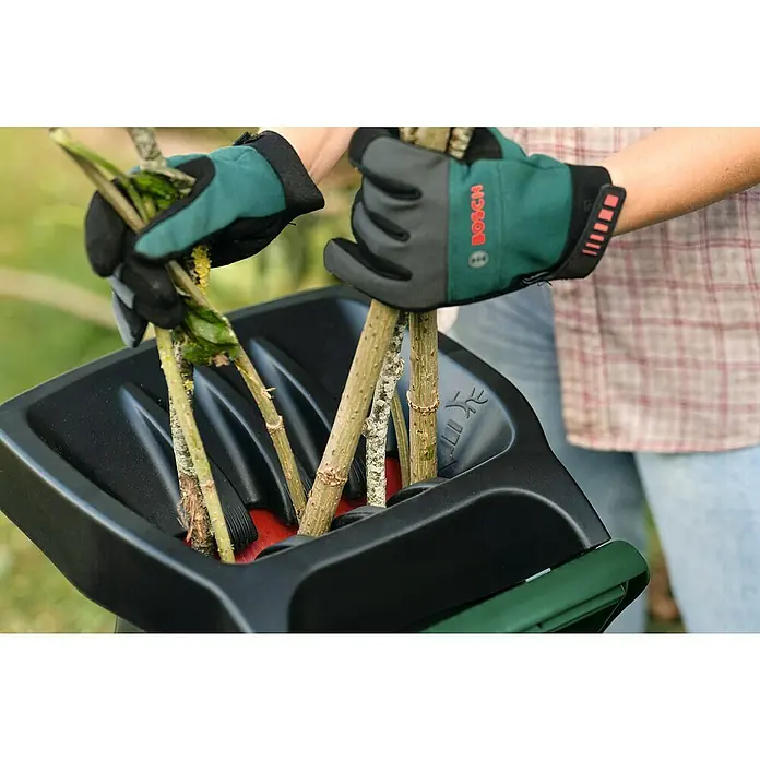 Bosch Elektro-Häcksler AXT RAPID 2200 - Max. Aststärke: 4 cm, 2.200 W - Eine Person benutzt einen Bosch-Gartenhäcksler, um Äste zu zerkleinern, und trägt dabei Handschuhe, um sich zu schützen.