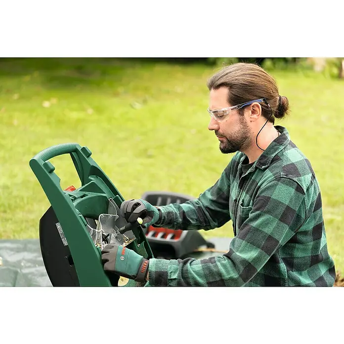 Bosch Elektro-Häcksler AXT RAPID 2200 - Max. Aststärke: 4 cm, 2.200 W - Ein Mann reinigt einen Bosch Gartenhäcksler, um die Klingen sauber zu halten. Der Häcksler ist grün und schwarz.