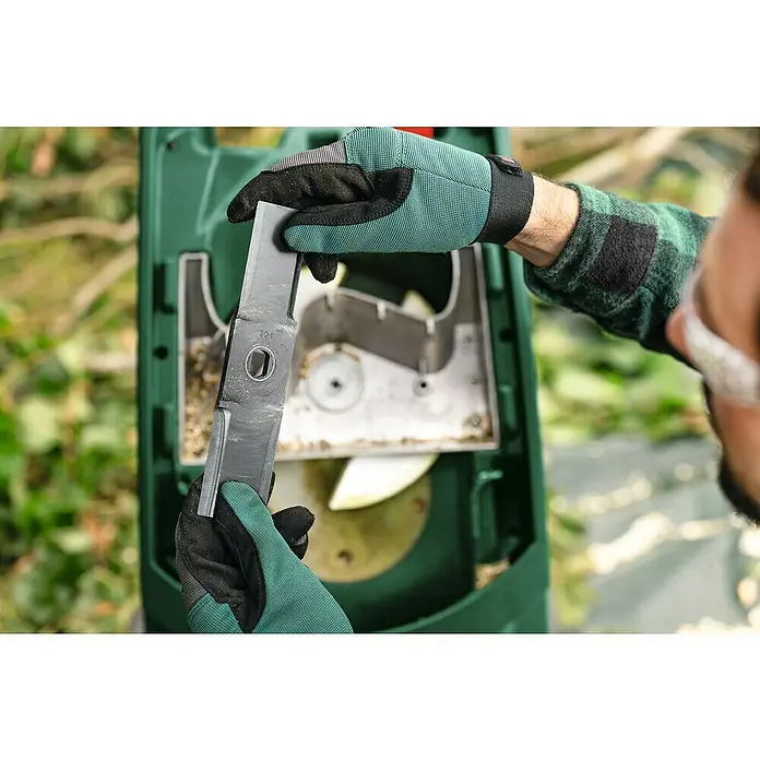 Bosch Elektro-Häcksler AXT RAPID 2200 - Max. Aststärke: 4 cm, 2.200 W - Eine Person mit Handschuhen inspiziert die Klinge eines Bosch-Gartengerätes vor dem Einsetzen. Wartung und Sicherheit im Fokus.