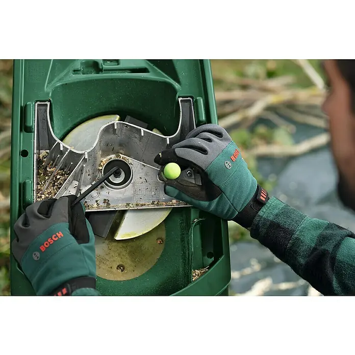 Bosch Elektro-Häcksler AXT RAPID 2200 - Max. Aststärke: 4 cm, 2.200 W - Eine Person, die eine Bosch Gartenhäckslersäubert, mit Schutzhandschuhen und einem Werkzeug, um Blockaden zu beseitigen.