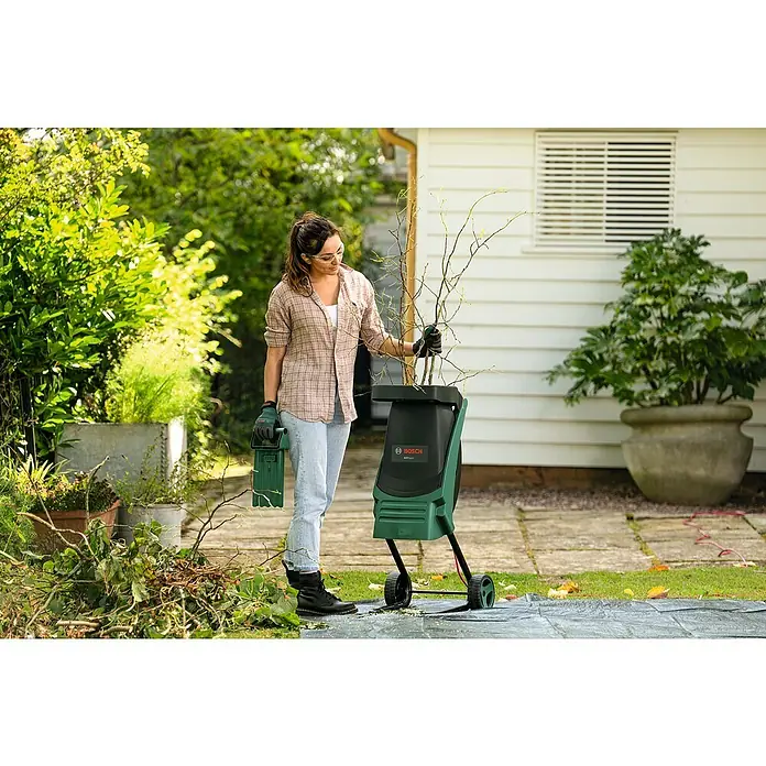 Bosch Elektro-Häcksler AXT RAPID 2200 - Max. Aststärke: 4 cm, 2.200 W - Eine Frau benutzt einen Bosch Gartenschredder im Garten, um Äste zu zerkleinern. Praktisch und effizient für die Gartenarbeit.