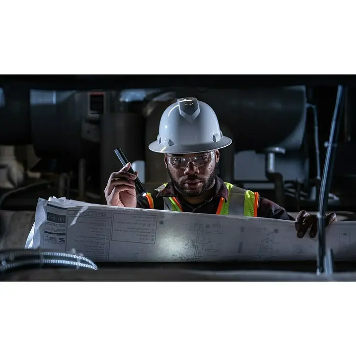 Ledlenser LED-Arbeitsleuchte W2 Work - L x B x H: 176 x 24 x 17 mm, Batteriebetrieben - Ein Bauarbeiter mit Schutzhelm und Sicherheitsweste studiert Pläne mit einer Taschenlampe, während er in einer industriellen Umgebung steht.