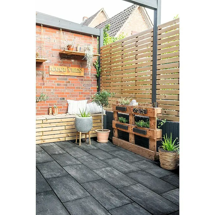Diephaus Terrassenplatte Dover - 60 x 40 x 4 cm, Graphit, Beton - Eine Terrasse mit dunklen Pflastersteinen, einer Holzbank und einem Hochbeet aus Paletten, dekoriert mit grünen Pflanzen für eine gemütliche Atmosphäre.