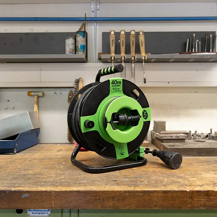 REV Kabeltrommel H05RR - Kunststoff, 40 m, H05RR-F, IP44 - Eine grüne und schwarze Kabeltrommel mit 40 Metern Kabel steht auf einer Werkbank. Das Kabel ist aufgerollt und bereit für den Einsatz.