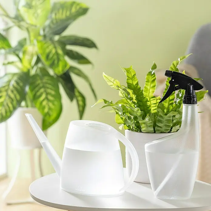 Scheurich Smilla Handsprüher - 0,7 l, Clear Pearl - Gießkanne und Sprühflasche auf einem Tisch, neben Pflanzen.