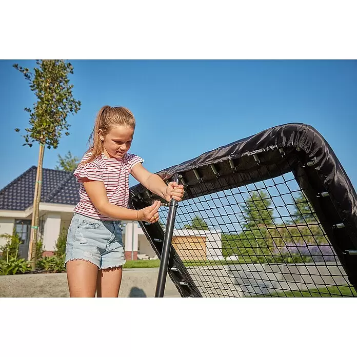 Salta Rebounder Motion - 84 x 84 cm, Schwarz - Mädchen justiert eine schwarze Trampolin-Sicherheitsumrandung mit Federn und Netz im Freien.