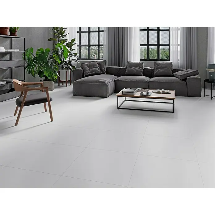 Feinsteinzeugfliese Super White - 59,8 x 59,8 cm, Weiß, Matt - Elegantes Wohnzimmer mit hellgrauen Fliesen, einem grauen Ecksofa, einem Holzsessel und großen Fenstern, die viel Licht hereinlassen.