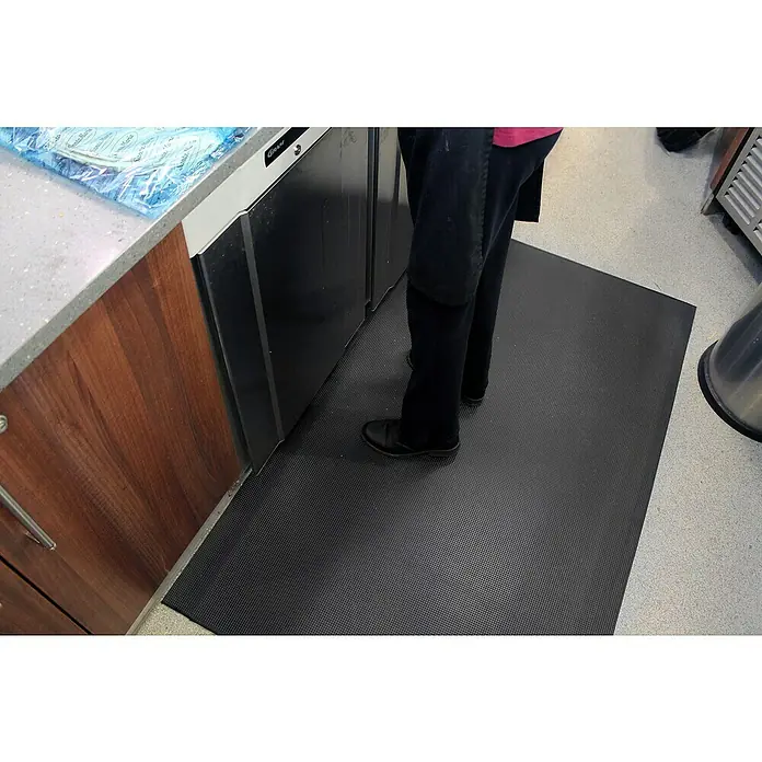 Coba Anti-Ermüdungsmatte Orthomat®-Ultimate90 x 60 cm, Schwarz - Eine rutschfeste Gummimatte in Schwarz liegt auf einem hellen Boden, die vor einer Kühltheke platziert ist und für mehr Sicherheit sorgt.