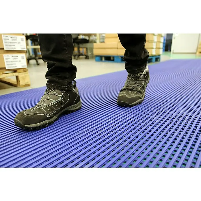 Coba Antirutschmatte DeckStepBlau, Breite: 100 cm, PVC - Die Aufnahme zeigt eine rutschfeste blaue Bodenmatte, die für mehr Sicherheit in Arbeitsbereichen konzipiert ist, mit einer Person, die darauf steht.