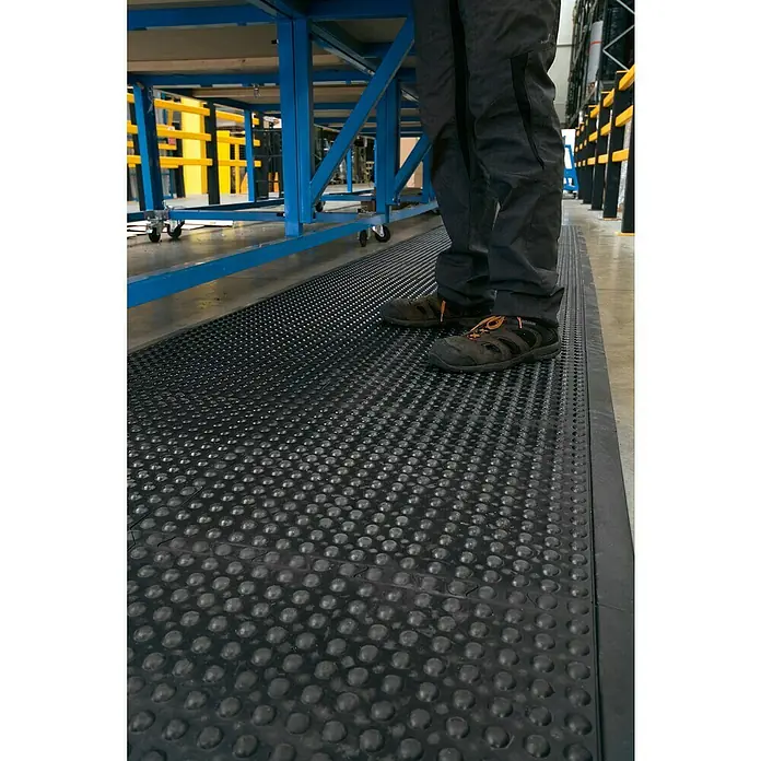 Coba Anti-Ermüdungsmatte Bubblemat Connect Mittelstück - 50 x 50 cm, Passend für: Coba Connect Seitenelement 28638625 / Eckelement 28638634 - Eine Anti-Ermüdungsmatte mit Noppenmuster bietet Komfort und Sicherheit am Arbeitsplatz, während eine Person darauf steht.