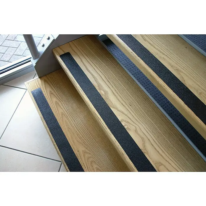 Coba Antirutschband Gripfoot Conformable - 183 x 2,5 cm, Schwarz - Nahaufnahme von Holztreppen mit schwarzen Antirutschstreifen für mehr Sicherheit. Ideal für den Innenbereich, um Stürze zu vermeiden.