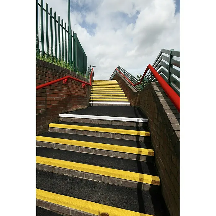 Coba Stufenmatte Grip® Stair Tread - Breite: 100 cm, Schwarz/Gelb - Gelb markierte Treppe mit rotem Geländer, die zu einer Fußgängerbrücke führt. Die Treppe ist mit rutschfestem Material ausgestattet.