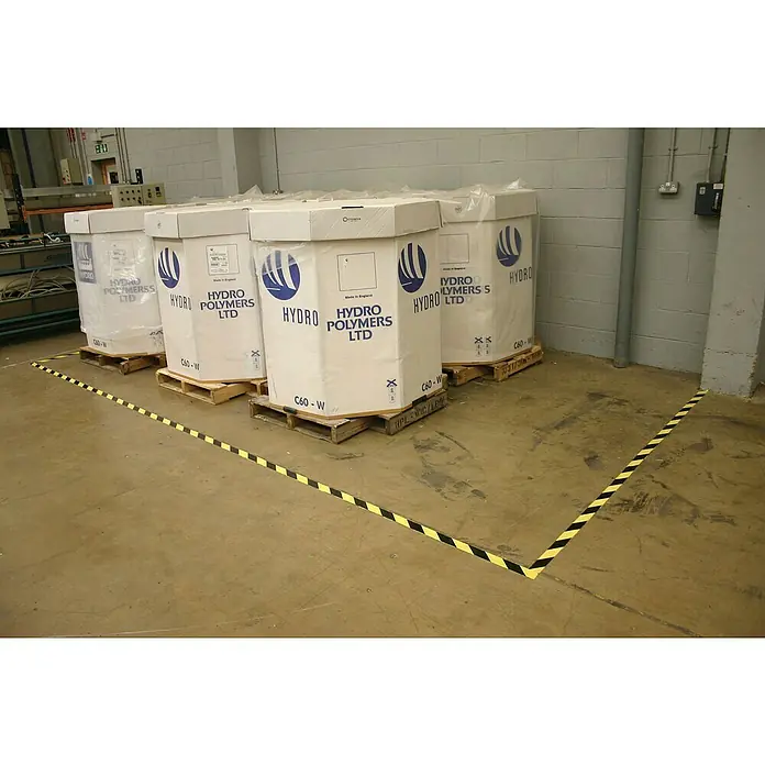 Coba Klebeband Markierband - Farbe: Schwarz / Gelb, 33 m x 5 cm - Mehrere weiße Hydro Polymers LTD-Behälter auf Paletten, umgeben von schwarz-gelbem Sicherheitsband.