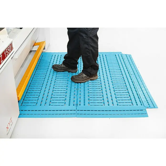 Coba Eckelement Work Deck - Schwarz, 11,2 x 11,2 cm, Passend für: Coba Work Deck Bodenrost 28938811 - Blaue modulare Bodenmatte mit einer Person, die darauf steht, neben einer Werkzeugmaschine.