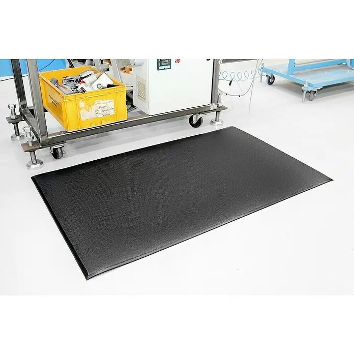 Coba Anti-Ermüdungsmatte Orthomat®-Premium - 90 x 60 cm, Schwarz - Schwarze Anti-Ermüdungsmatte auf einem sauberen, weißen Industrieboden. Die strapazierfähige Matte bietet Komfort und reduziert die Belastung bei längerem Stehen.