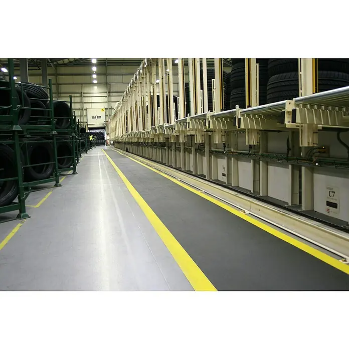 Coba Anti-Ermüdungsmatte Orthomat®-Standard Safety - Breite: 90 cm, Schwarz / Gelb - Regale voller Reifen in einer Fabrikhalle mit gelb markiertem Boden. Die Reifen lagern aufgestapelt und sind zur Auslieferung bereit.