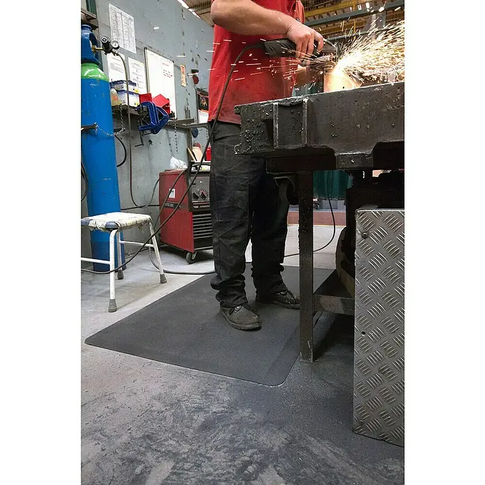 Coba Anti-Ermüdungsmatte Diamond Tread Meterware - Breite: 90 cm - Arbeiter benutzt eine Schleifmaschine auf einer Werkstattmatte. Die Matte bietet Komfort und Sicherheit am Arbeitsplatz durch Rutschfestigkeit.