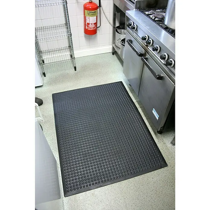 Coba Anti-Ermüdungsmatte Bubblemat Nitril - 120 x 90 cm, Ölbeständig - Eine rutschfeste, schwarze Gummimatte mit Noppen liegt auf dem Boden einer Großküche, um die Sicherheit zu erhöhen.