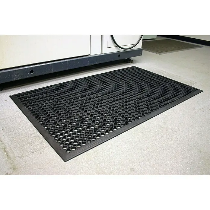 Coba Ringmatte Rampmat - 150 x 90 cm, Schwarz - Schwarze Gummimatte mit Löchern vor einer Maschine.