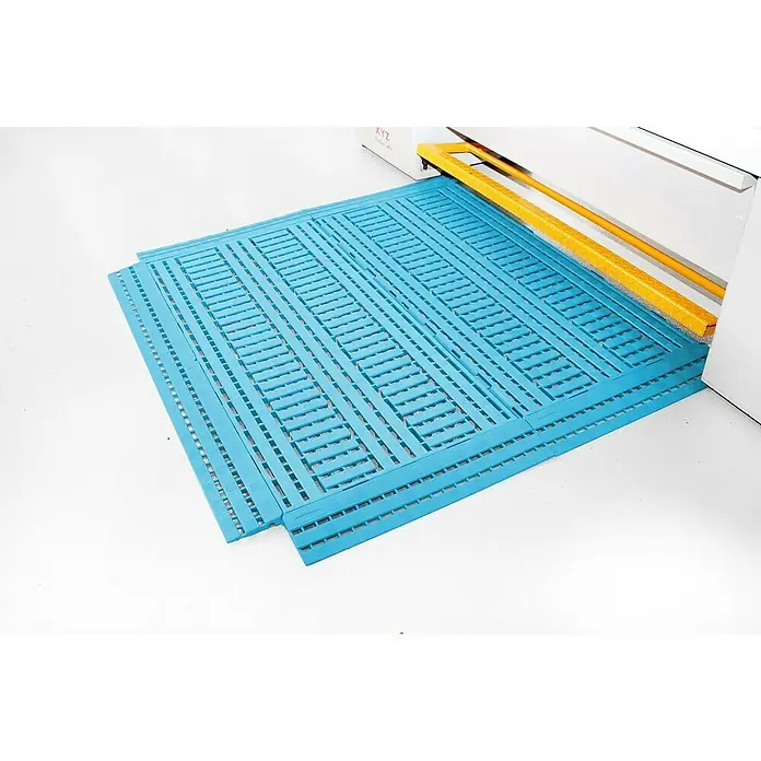 Coba Bodenrost Work Deck - Blau, 60 x 120 cm - Ein blaues, modulares Bodenbelagsystem liegt vor einer Maschine. Das System ist perforiert und scheint aus Kunststoff zu sein.