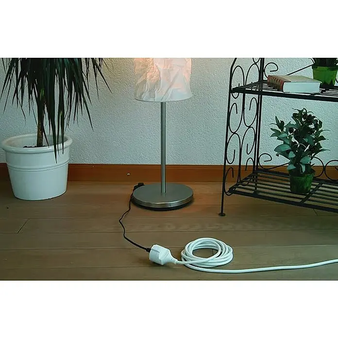 Chacon Alargador - 5 m, Blanco, H05VV-F - Una foto de interior muestra una lámpara de pie con un cable enredado, junto a plantas en macetas y una estantería decorativa.