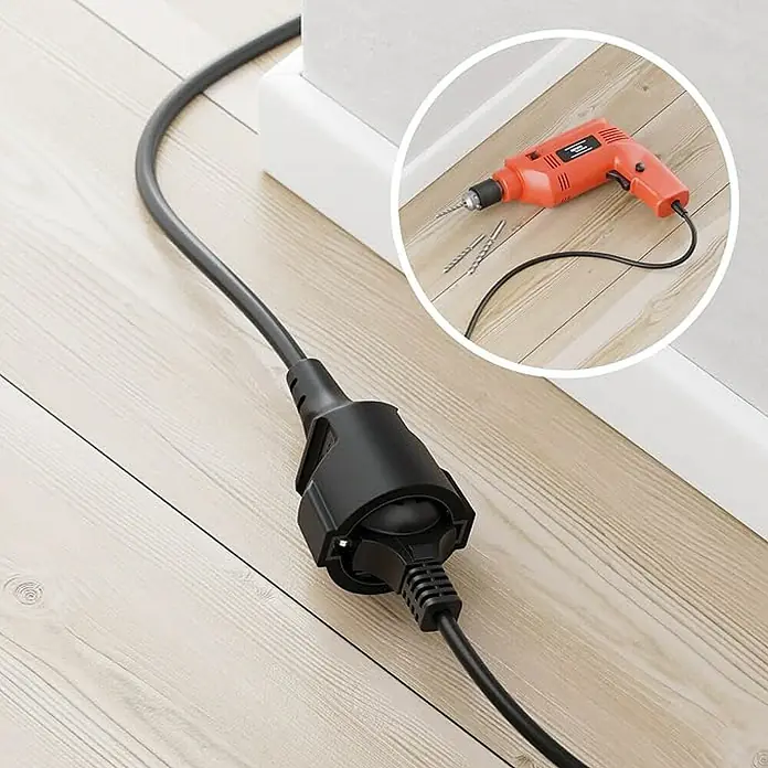 Chacon Alargador - 5 m, Negro, H05VV-F - Primer plano de un cable de extensión en un suelo de madera con un taladro al fondo, utilizado para trabajos de construcción y bricolaje.