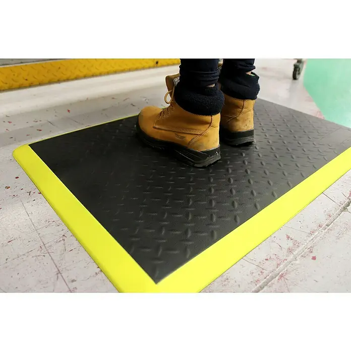 Coba Anti-Ermüdungsmatte Elite® Diamond60 x 90 cm, Schwarz/Gelb - Arbeitsschuhe auf einer schwarzen, gelb umrandeten Anti-Ermüdungsmatte. Optimal für Komfort und Sicherheit am Arbeitsplatz.