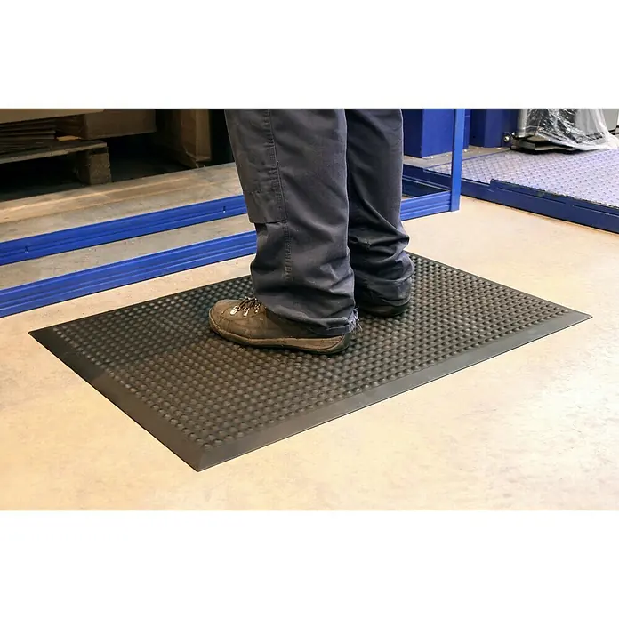 Coba Anti-Ermüdungsmatte Elite® ESD - 90 x 120 cm, Einsatzbereich: Elektrobetriebe - Eine Person steht auf einer schwarzen Anti-Ermüdungsmatte mit Noppenmuster in einer industriellen Umgebung.