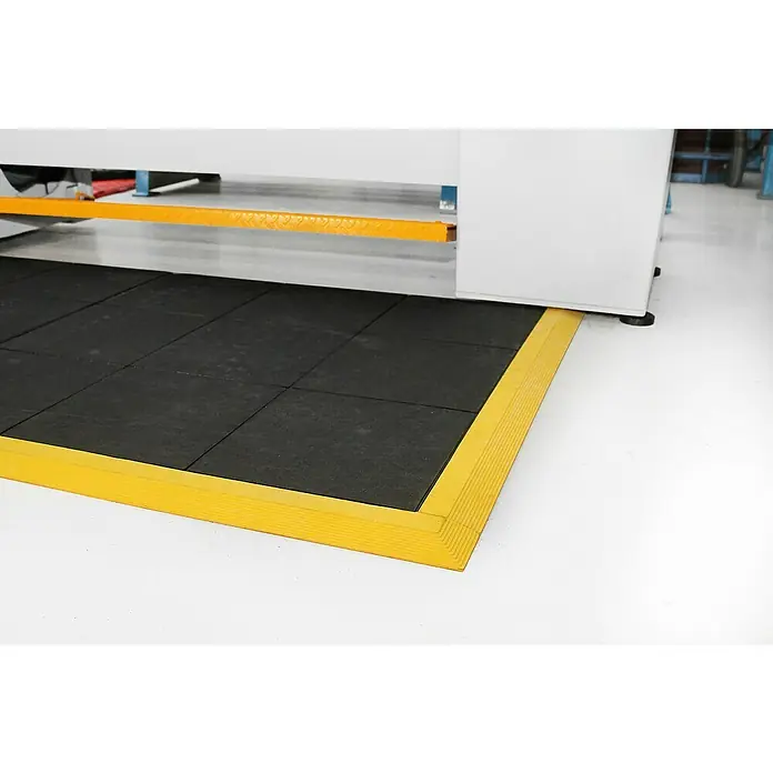 Coba Anti-Ermüdungsmatte Fatigue-Step90 x 90 cm, Einsatzbereich: Industrie - Schwarze Gummimatten mit gelbem Rand unter einer weißen Maschine.
