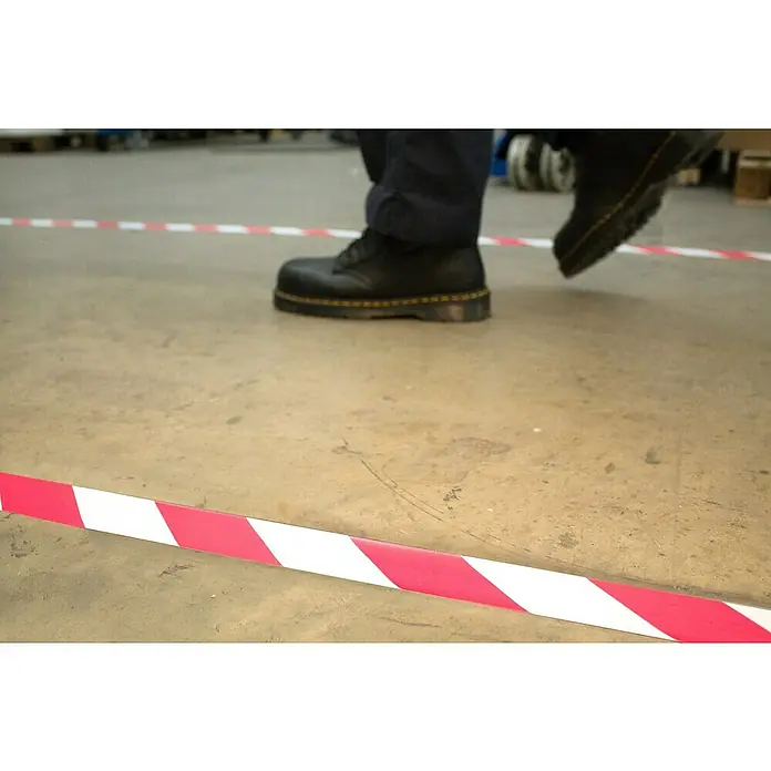 Coba Klebeband Markierband - Farbe: Rot / Weiß, 33 m x 5 cm - Ein Paar schwarze Dr. Martens-Stiefel überqueren ein rot-weißes Absperrband auf einem Betonboden. Robuste Schuhe im Fokus.