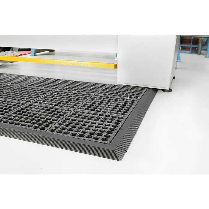 Coba Anti-Ermüdungsmatte Fatigue-Step Grit Top - 90 x 90 cm, Gelochte Oberfläche - Ein grauer, modularer Bodenbelag mit Löchern bedeckt einen Industrieboden, der Komfort und Sicherheit bietet. Ideal für Arbeitsplätze.