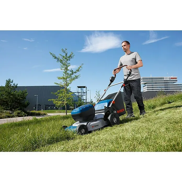 Bosch Professional AMPShare 18V Akku-Rasenmäher GRA 18V2-46 - 18 V, Ohne Akku, Schnittbreite: 46 cm - Ein Mann schiebt einen blauen Bosch Akku-Rasenmäher den Rasen hinauf. Im Hintergrund sind Büros zu sehen.
