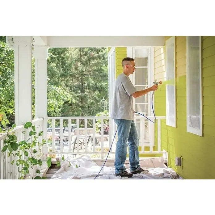 Graco Magnum Juego de recambio FlexLiner - Específico para: Graco Magnum Sistema de pulverización Compact A5DS - Un hombre usa un pulverizador de pintura para aplicar un color amarillo vibrante en el exterior de una casa, de pie en un porche cubierto.