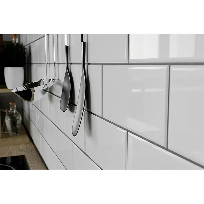 Modern Style Wandfliese Alboran Blanco - 7,5 x 15 cm, Weiß, Glänzend - Nahaufnahme von glänzenden weißen Keramikfliesen an einer Küchenwand, akzentuiert durch elegante Küchenutensilien aus Edelstahl.